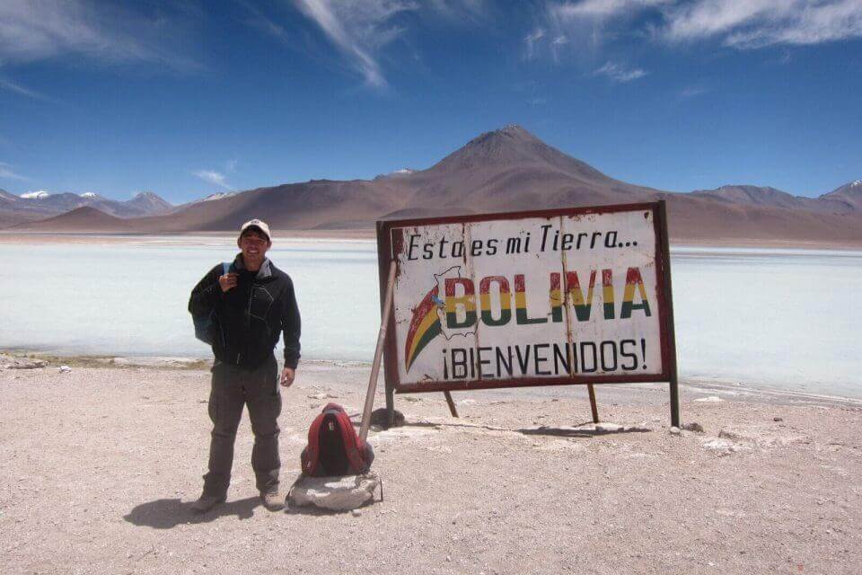 A man standing in front of a sign that says "Bolivia" in GALÀ, a travel book celebrating wanderlust.