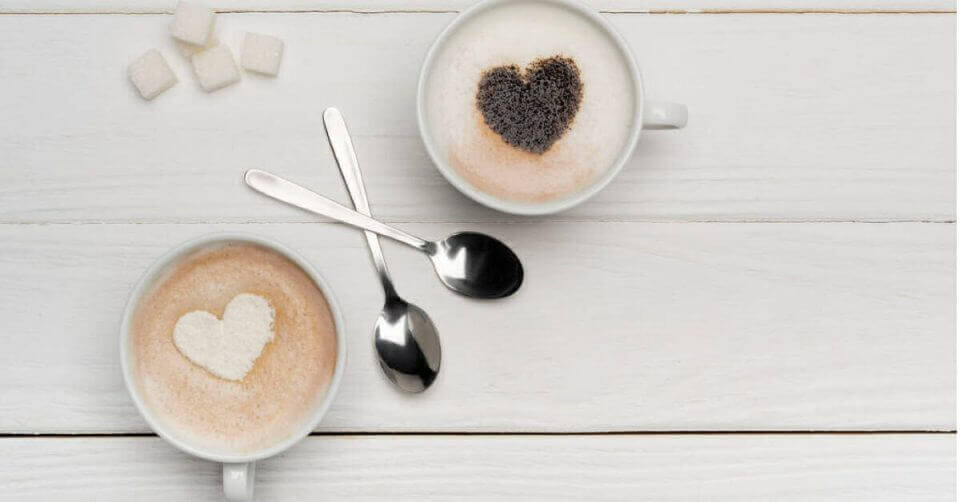 Celebrate International Coffee Day with two cups of coffee adorned with a heart shaped sugar.