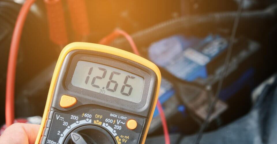 A person using a multimeter to identify the battery terminals on a car.