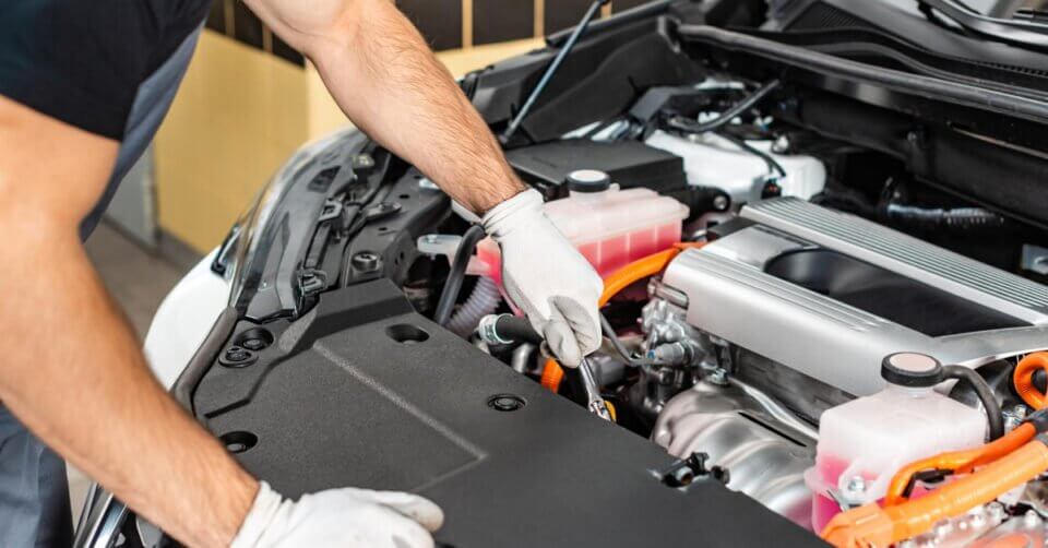 A man is working on the engine of a car while contemplating how to buy a new car.
