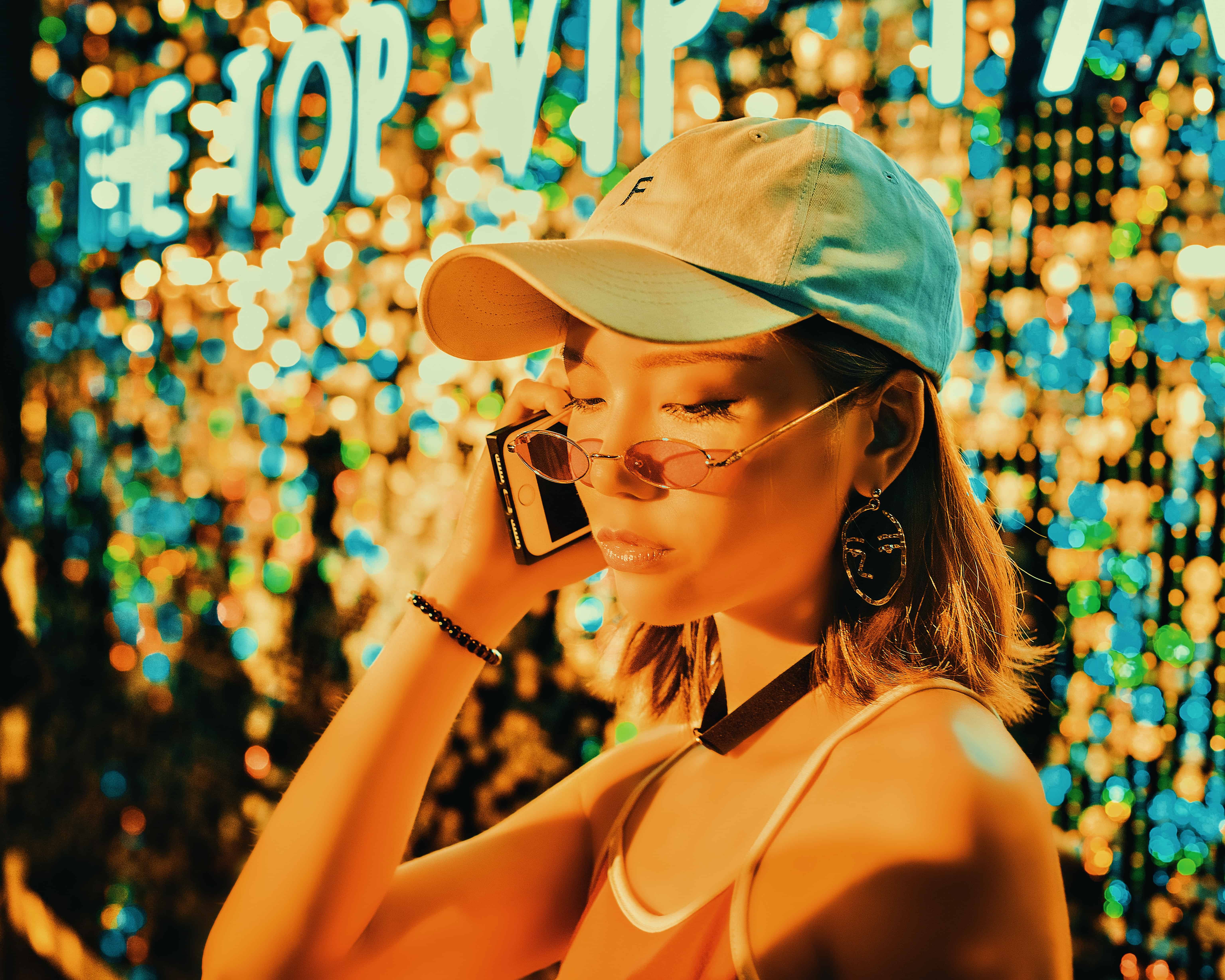 A woman in a cap and sunglasses talks on her TM prepaid phone against a colorful, illuminated backdrop at night.