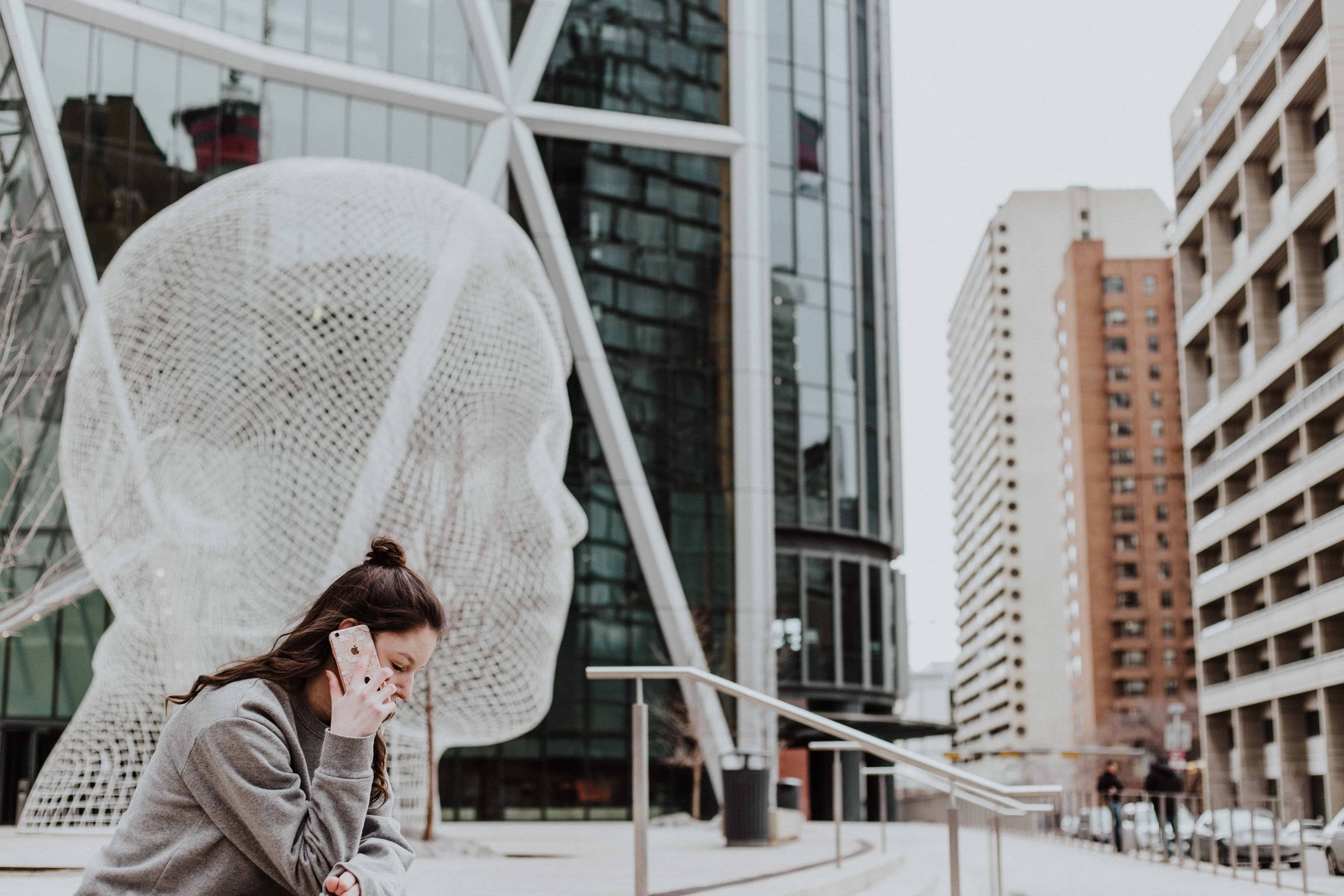 A woman talks on her TM prepaid number, standing near a large wireframe head sculpture against the backdrop of modern urban architecture.