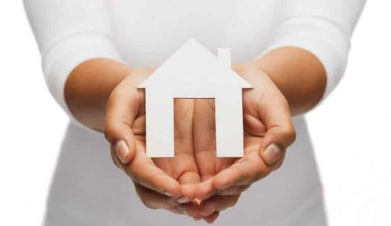 A woman holding a paper house and considering if getting a home warranty is really sulit.