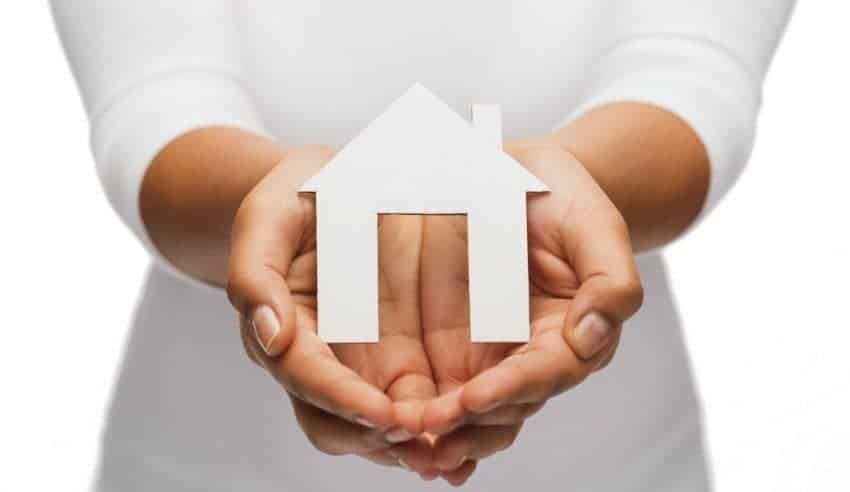 A woman holding a paper house and considering if getting a home warranty is really sulit.