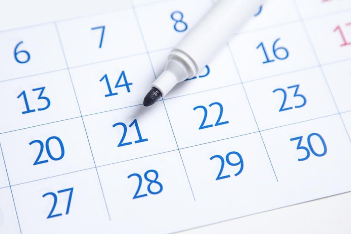 A close-up image of a 2025 Social Media Holiday Calendar showing the days of a month. The dates are in blue, except for weekends, which are in red. A white marker with its cap removed rests on "21," indicating it might be of importance. The days are printed in a grid layout, reminiscent of typical calendars used in the Philippines.