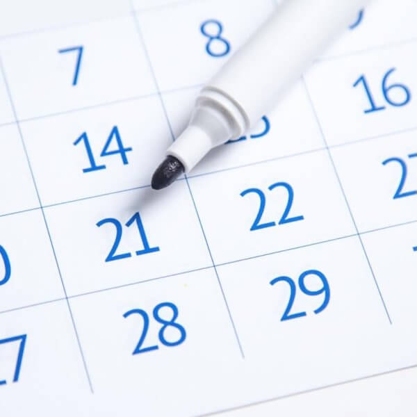 A close-up image of a 2025 Social Media Holiday Calendar showing the days of a month. The dates are in blue, except for weekends, which are in red. A white marker with its cap removed rests on "21," indicating it might be of importance. The days are printed in a grid layout, reminiscent of typical calendars used in the Philippines.