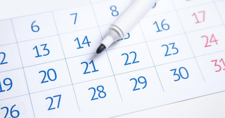 A close-up image of a 2025 Social Media Holiday Calendar showing the days of a month. The dates are in blue, except for weekends, which are in red. A white marker with its cap removed rests on "21," indicating it might be of importance. The days are printed in a grid layout, reminiscent of typical calendars used in the Philippines.