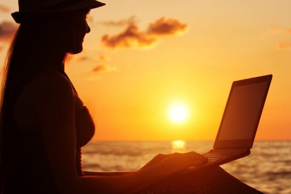 A woman is sitting on the beach with her laptop, enjoying the sunset in Siargao.