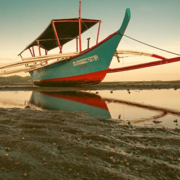 Beached traditional boat at low tide with reflection on water during Summer Break.