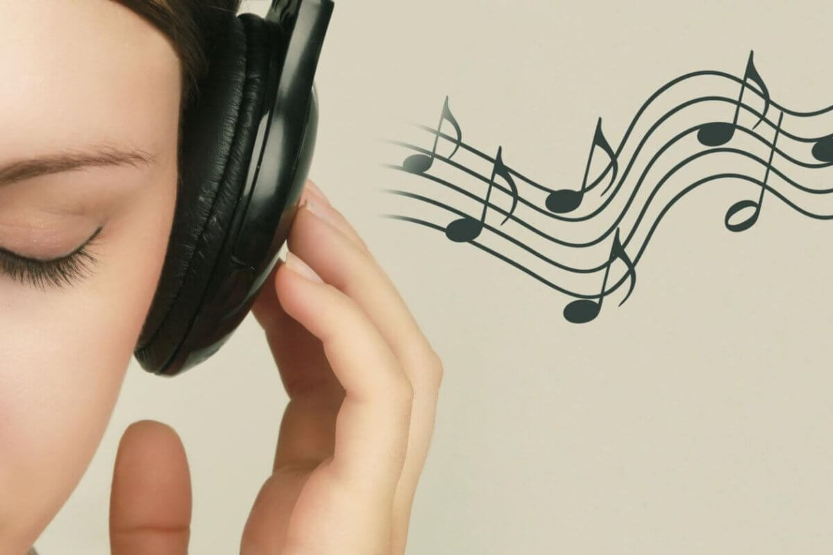 Close-up of a person with closed eyes wearing black headphones, holding the left earcup with their left hand. To the right, musical notes on a staff float against a light beige background, suggesting they are enjoying the Best OPM Songs. Only the left side of the person's face is visible.