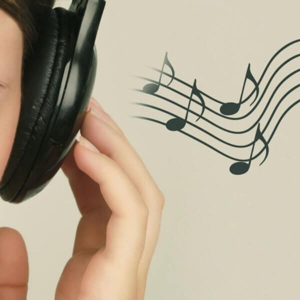 Close-up of a person with closed eyes wearing black headphones, holding the left earcup with their left hand. To the right, musical notes on a staff float against a light beige background, suggesting they are enjoying the Best OPM Songs. Only the left side of the person's face is visible.