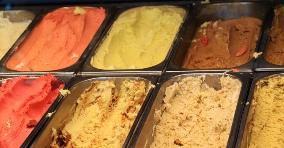 A display of various flavors of gelato arranged in metal trays at one of the best gelato places in Metro Manila, featuring vibrant colors ranging from pink to beige. The gelato's creamy texture is highlighted by the soft ripples and peaks visible on the surface.