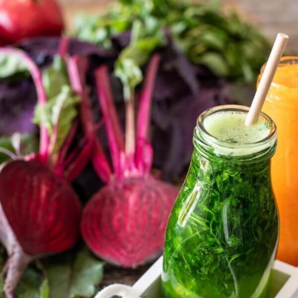 Three bottles of colorful vegetable juices—green, beetroot red, and orange—from top juice bars in Metro Manila, placed on a wooden table, surrounded by fresh vegetables like beets, carrots, and leafy greens.