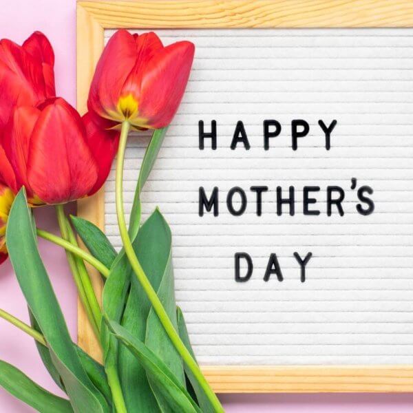 A Mother's Day celebration greeting with red tulips alongside a framed white letter board that reads "happy mother's day" on a pink background.