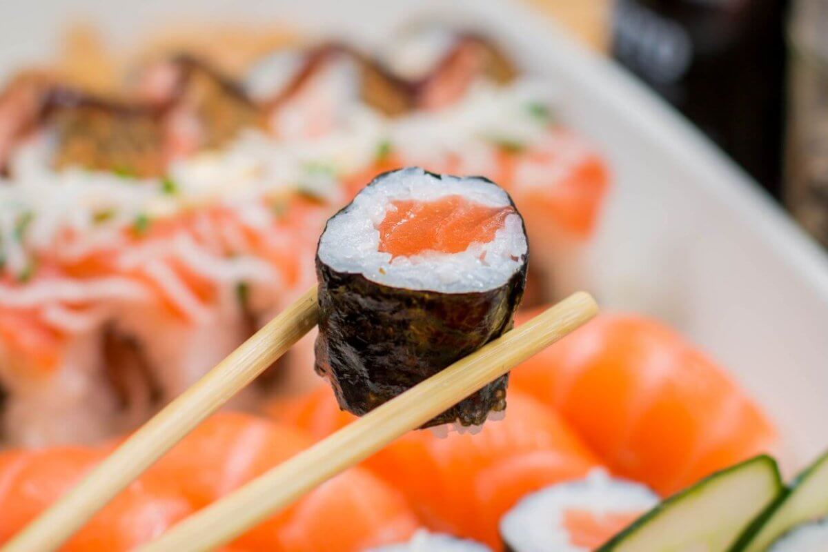 Close-up of chopsticks holding a sushi roll with a seaweed wrap, rice, and salmon filling. The background showcases various sushi pieces, including nigiri topped with raw salmon slices. This arrangement highlights the vibrant colors and freshness of Metro Manila's best Japanese restaurants.