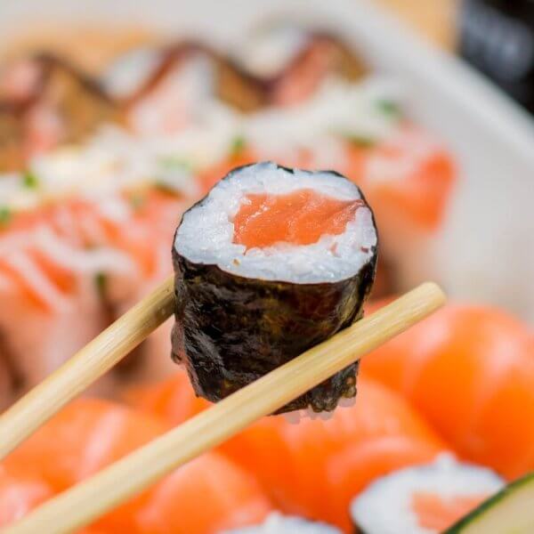 Close-up of chopsticks holding a sushi roll with a seaweed wrap, rice, and salmon filling. The background showcases various sushi pieces, including nigiri topped with raw salmon slices. This arrangement highlights the vibrant colors and freshness of Metro Manila's best Japanese restaurants.