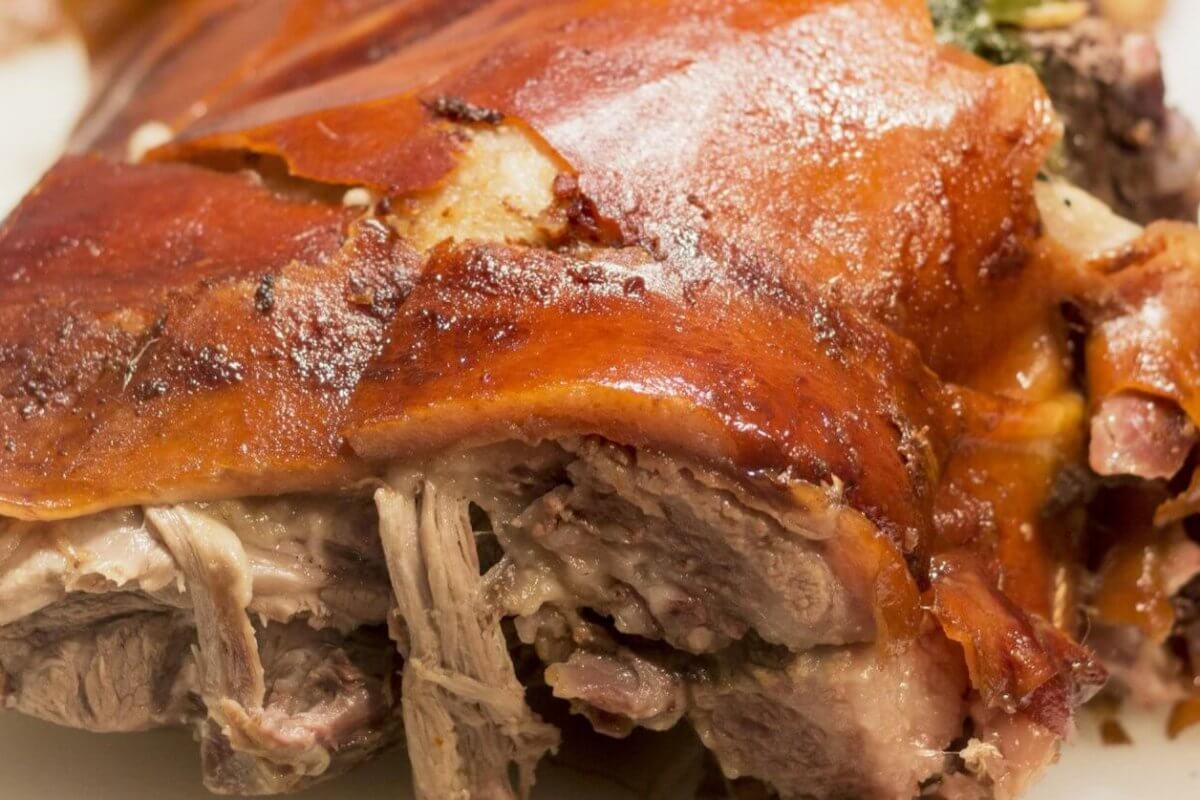 A close-up of a roasted pork dish from one of the best restaurants in Alabang, showcasing crispy, golden-brown skin with some tender, juicy shredded meat visible underneath. The meat appears well-cooked and succulent, with a slightly charred, flavorful exterior. The plain white background highlights the dish's texture. 