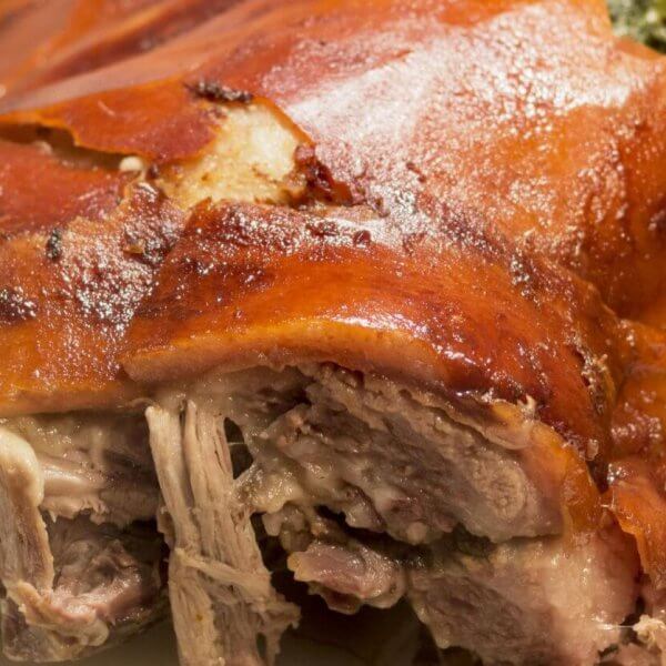 A close-up of a roasted pork dish from one of the best restaurants in Alabang, showcasing crispy, golden-brown skin with some tender, juicy shredded meat visible underneath. The meat appears well-cooked and succulent, with a slightly charred, flavorful exterior. The plain white background highlights the dish's texture.
