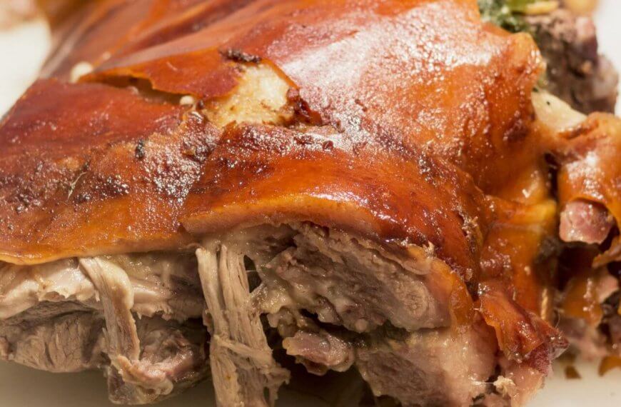 A close-up of a roasted pork dish from one of the best restaurants in Alabang, showcasing crispy, golden-brown skin with some tender, juicy shredded meat visible underneath. The meat appears well-cooked and succulent, with a slightly charred, flavorful exterior. The plain white background highlights the dish's texture. 