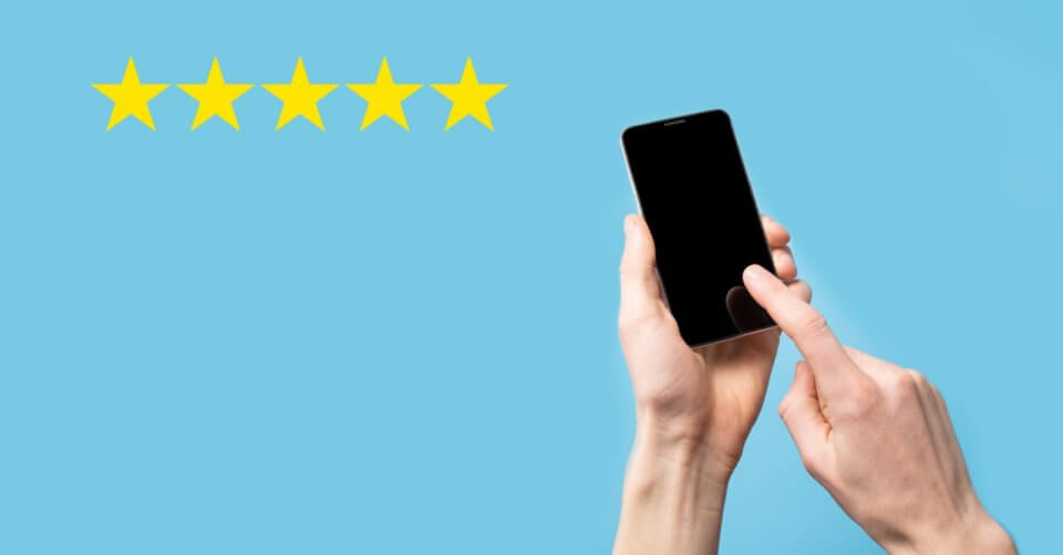 Hands holding a smartphone with one finger touching the screen against a light blue background. To the left, five yellow stars line up horizontally, showcasing a five-star rating—an ideal visual for any new phone buying guide. The smartphone screen remains blank and black.