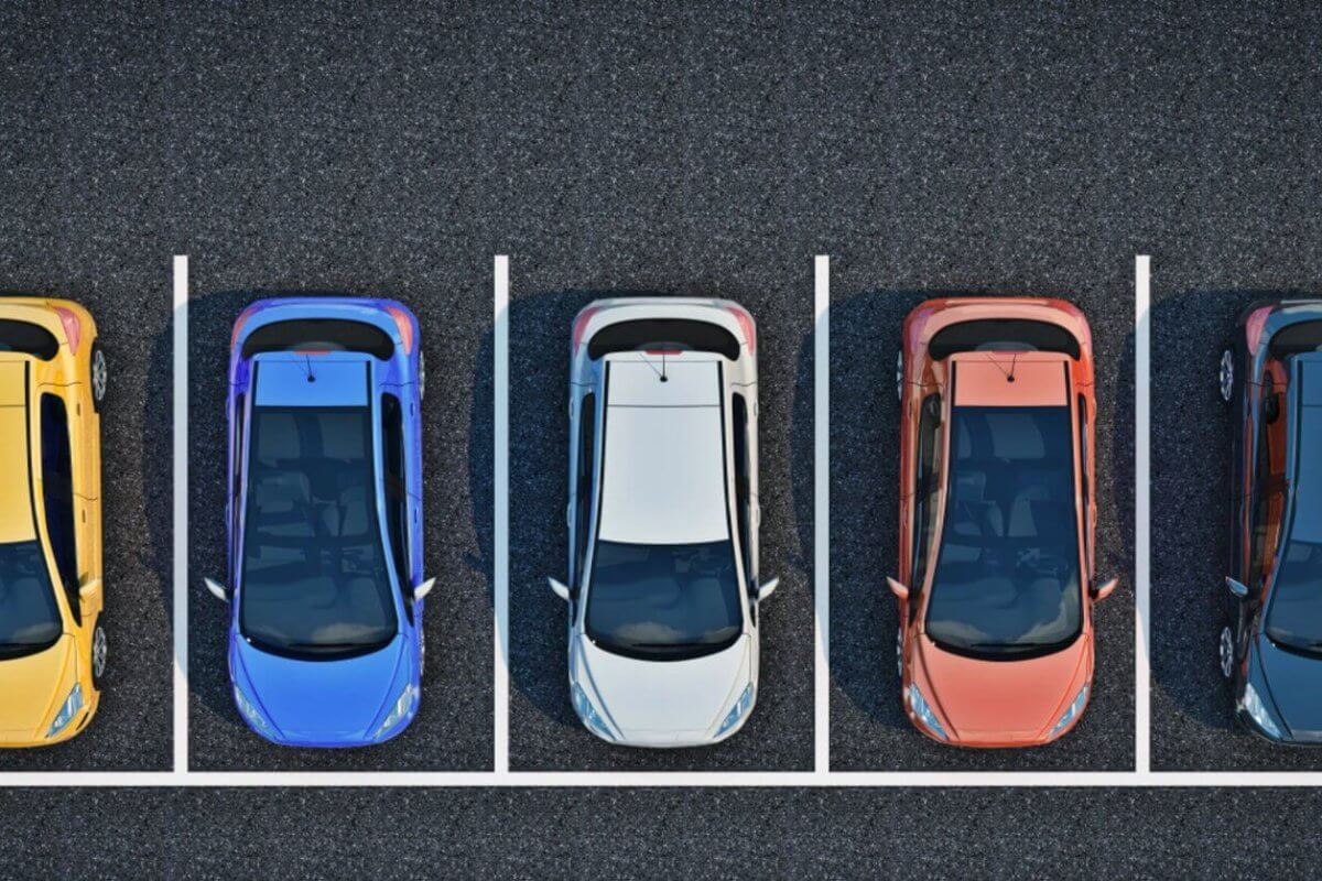 A top-down view of a parking lot shows five cars parked in a row, each in separate parking spots. The cars are, from left to right, yellow, blue, white, red, and black. The parking spots are outlined with white lines on the asphalt surface. It's a BGC designed for a stress-free experience.
