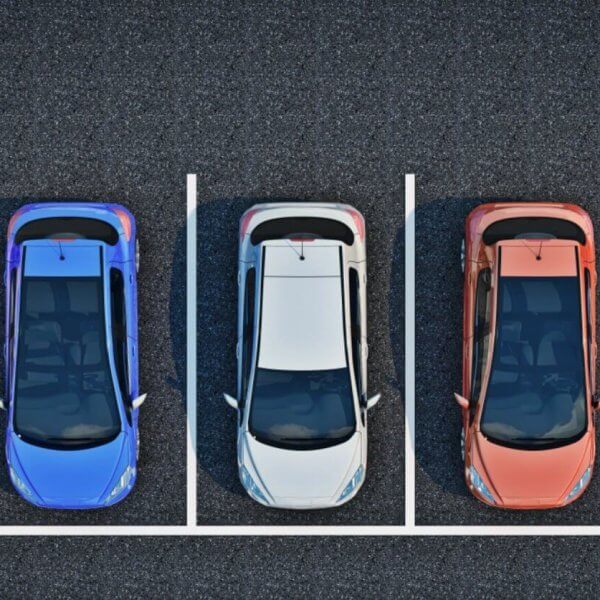 A top-down view of a parking lot shows five cars parked in a row, each in separate parking spots. The cars are, from left to right, yellow, blue, white, red, and black. The parking spots are outlined with white lines on the asphalt surface. It's a BGC designed for a stress-free experience.