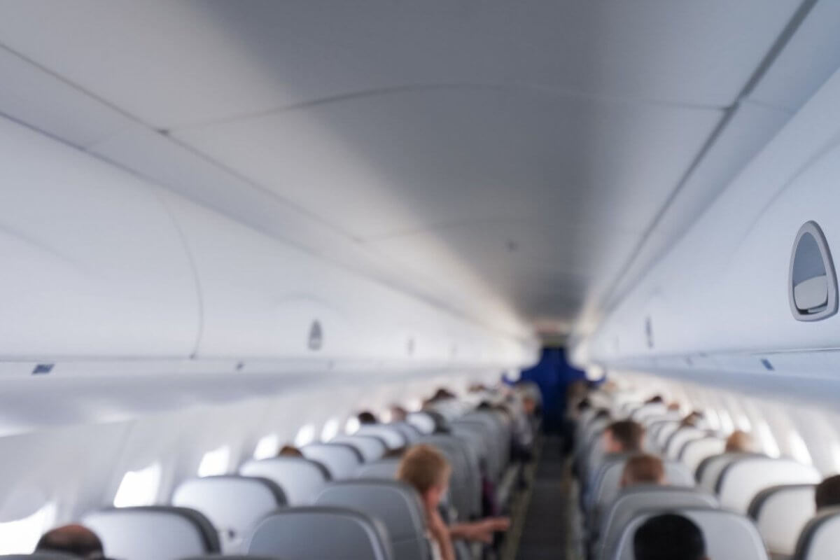 The interior of an airplane cabin with rows of occupied seats on a Cebu Pacific flight. The image shows overhead compartments closed and passengers are seated, facing forward towards the front of the plane. The lighting is bright, creating a clean and modern look. The distant cockpit area is visible but not detailed.