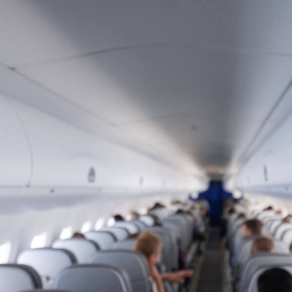 The interior of an airplane cabin with rows of occupied seats on a Cebu Pacific flight. The image shows overhead compartments closed and passengers are seated, facing forward towards the front of the plane. The lighting is bright, creating a clean and modern look. The distant cockpit area is visible but not detailed.