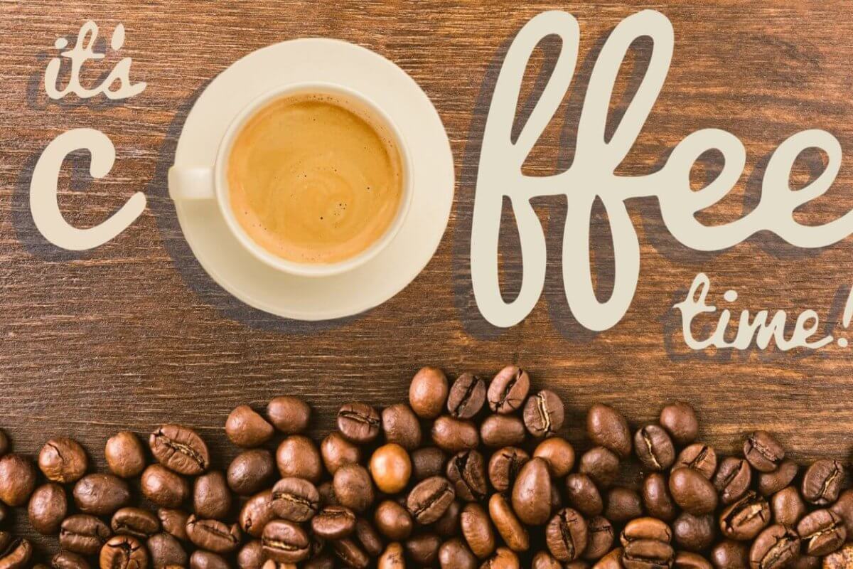A white cup of coffee sits on a wooden surface, surrounded by scattered coffee beans. The words "it's coffee time!" are artistically written in beige lettering around the cup. The composition creates a cozy and inviting atmosphere that celebrates Antipolo's best coffee shops.