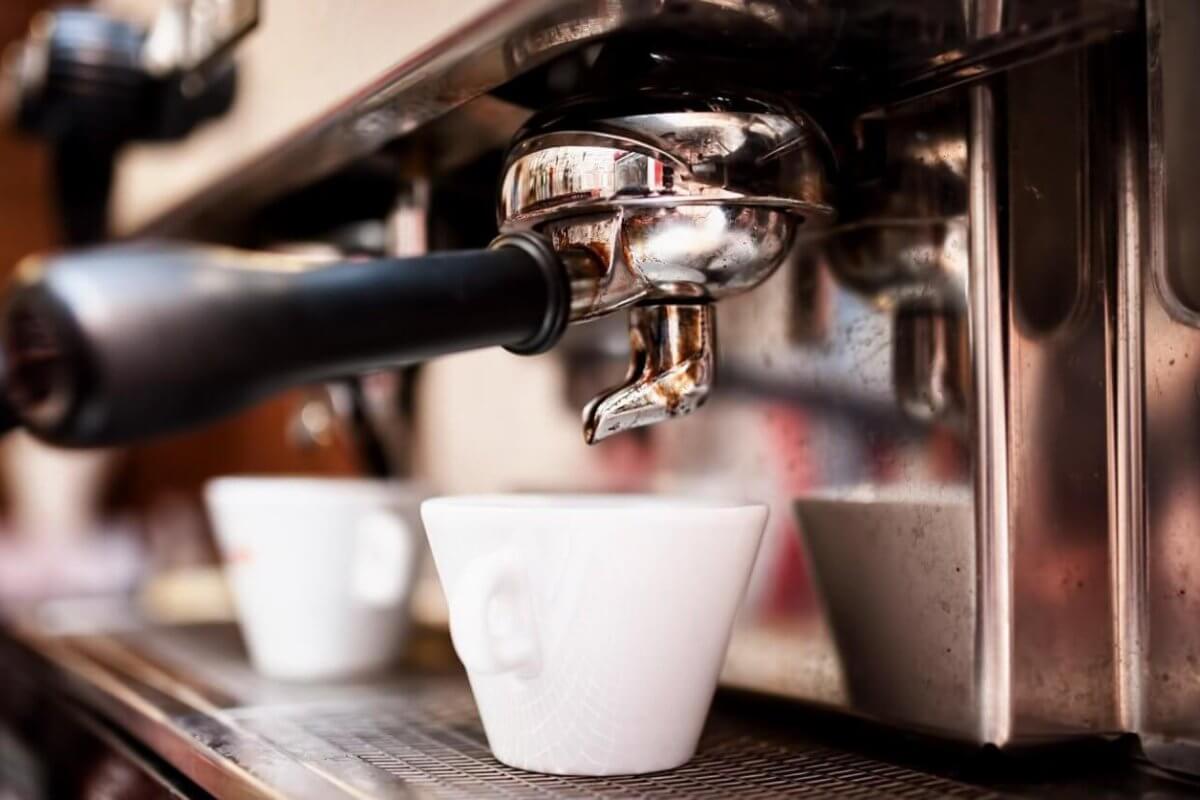 Close-up of a professional espresso machine in action, with a portafilter and spout dispensing coffee into a white ceramic cup below. The shiny metal surface of the machine reflects the bustling environment, hinting at Davao's best coffee place—a must-try for any café enthusiast.