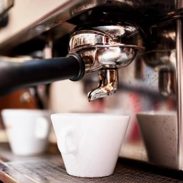 Close-up of a professional espresso machine in action, with a portafilter and spout dispensing coffee into a white ceramic cup below. The shiny metal surface of the machine reflects the bustling environment, hinting at Davao's best coffee place—a must-try for any café enthusiast.