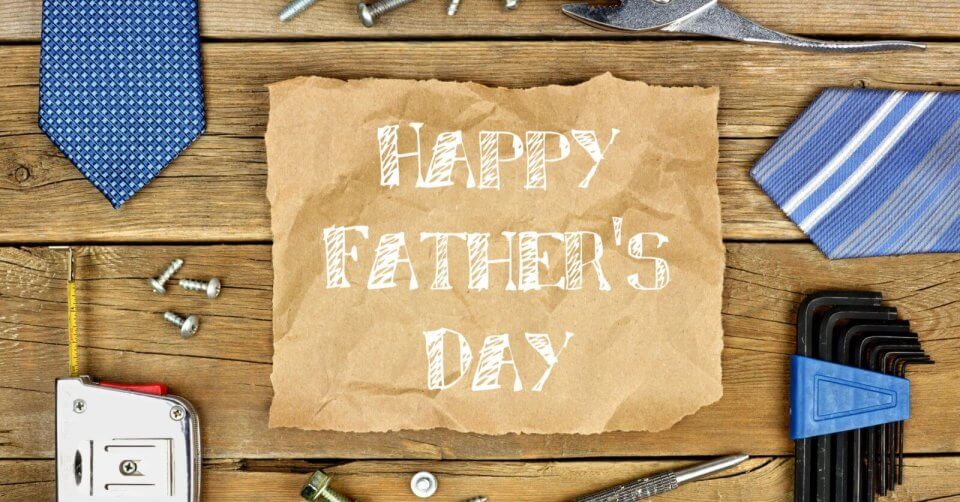 A textured wooden table holds an array of tools like a wrench, screws, nails, measuring tape, and Allen wrenches. Two blue-patterned ties are arranged diagonally. In the center lies brown paper with "Happy Father's Day" in bold white font—perfect for heartfelt messages and gift ideas.