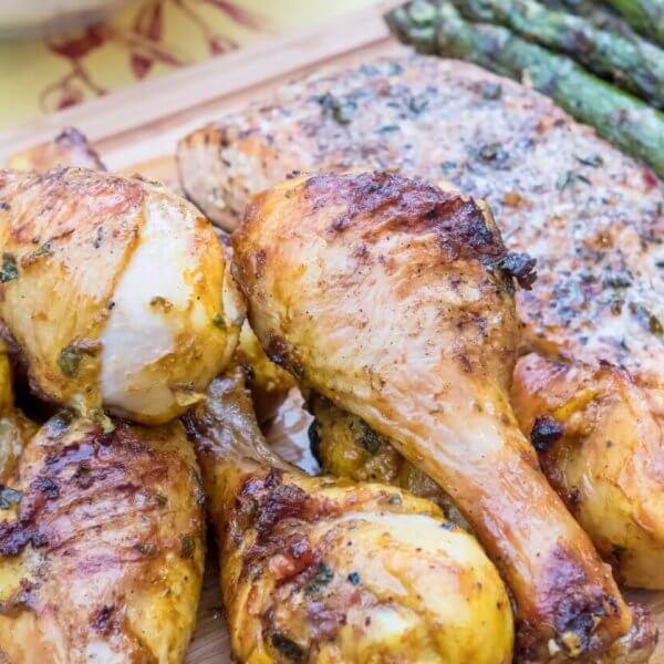 Grilled chicken drumsticks, seasoned and charred, are arranged in the foreground on a wooden board, alongside a piece of herb-topped inihaw fish. To the side, there's a row of grilled asparagus spears, adding a vibrant green contrast to this delightful dish reminiscent of popular hotspots in Metro Manila.