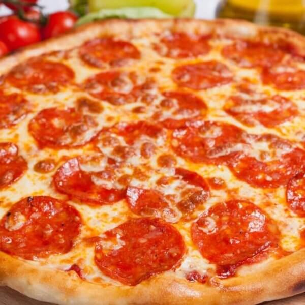 A freshly baked pepperoni pizza with a golden-brown crust is displayed on a wooden board. The pizza, reminiscent of what you might find at top restaurants, is topped with melted cheese and an uneven spread of pepperoni slices. Ingredients like tomatoes, peppers, cheese, and oil bottles are blurred in the background.