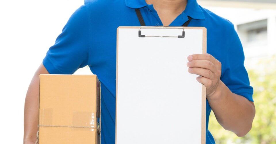 A delivery person in a blue shirt holds a cardboard box in one hand and presents a blank clipboard in the other, set against a background subtly hinting at Metro Manila's greenery. The focus on the clipboard and box suggests a delivery or package signing scenario, perhaps linked to Lazada Drop-off Points.