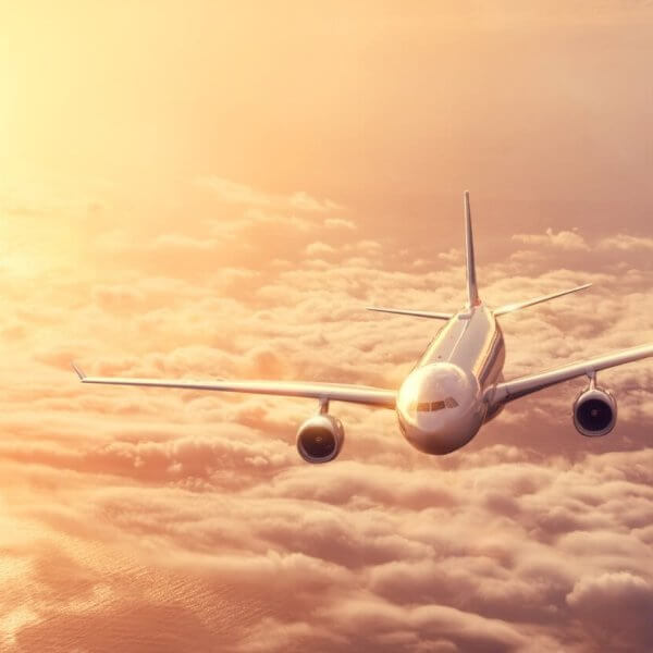 A commercial airplane from Philippine Airlines flies above a dense layer of clouds during sunset. The sky is filled with warm hues of orange and yellow, casting a golden glow on the plane and clouds. The airplane is heading toward the camera, with both wings and engines visible.