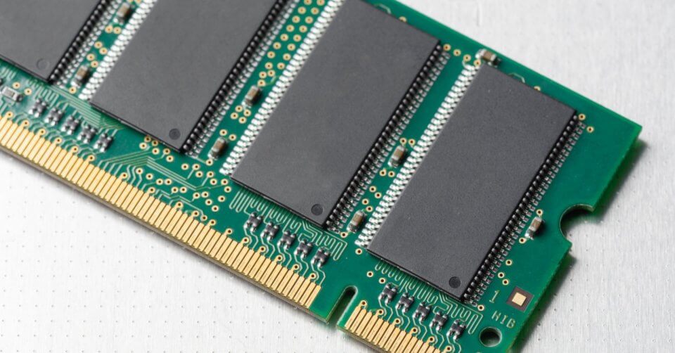 Close-up of a green RAM stick with black memory chips and visible circuit pathways, akin to selecting the right components from a phone buying guide. The gold connector pins glisten at the bottom as it rests on a light, textured surface.