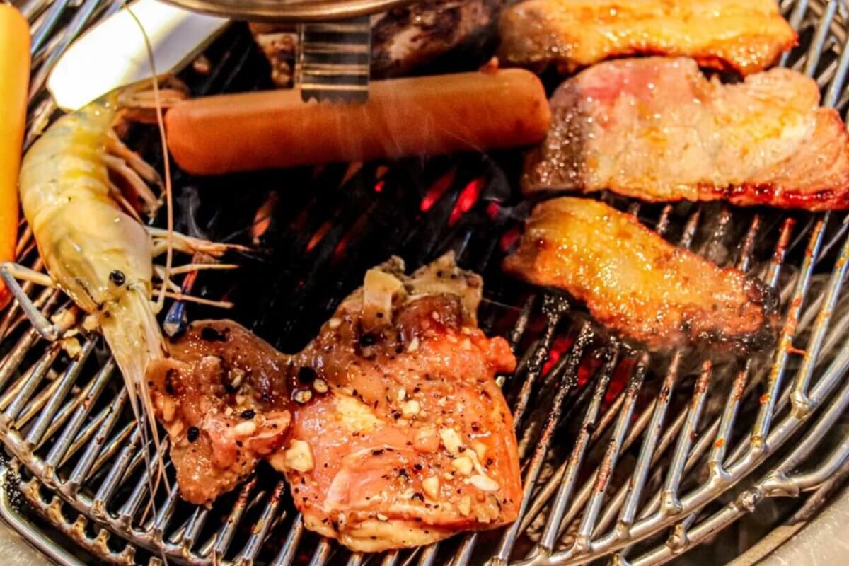 A grill loaded with various foods, including shrimp, sausage, and assorted cuts of Samgyupsal, all with visible seasoning. The grill grates have a shiny, metallic look as the food items cook to perfection, displaying grill marks and a slight char—a mouthwatering feast that could easily be found in Metro Manila.
