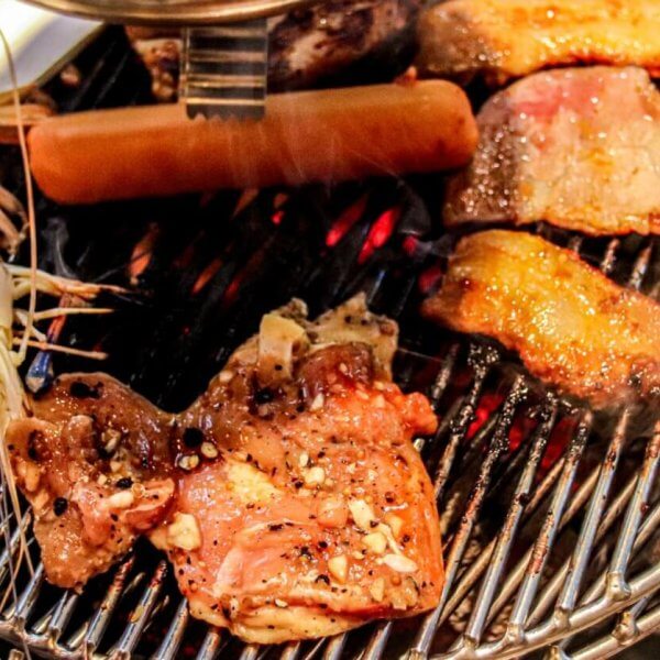 A grill loaded with various foods, including shrimp, sausage, and assorted cuts of Samgyupsal, all with visible seasoning. The grill grates have a shiny, metallic look as the food items cook to perfection, displaying grill marks and a slight char—a mouthwatering feast that could easily be found in Metro Manila.