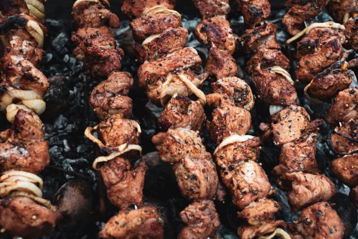 Several skewers of marinated meat and onions are being grilled over a bed of charcoal. The meat is slightly charred, giving it a deliciously cooked look with visible spices and seasoning. The skewers are spaced closely together, filling up the grill surface—just like you'd find at the best restaurants in Tomas Morato.