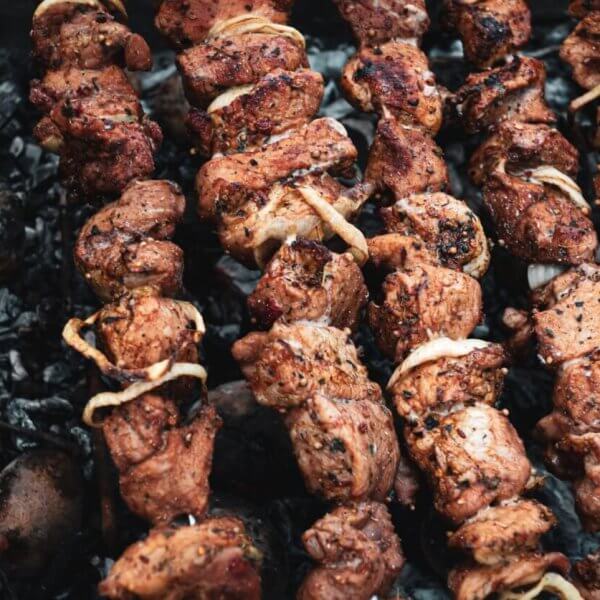 Several skewers of marinated meat and onions are being grilled over a bed of charcoal. The meat is slightly charred, giving it a deliciously cooked look with visible spices and seasoning. The skewers are spaced closely together, filling up the grill surface—just like you'd find at the best restaurants in Tomas Morato.