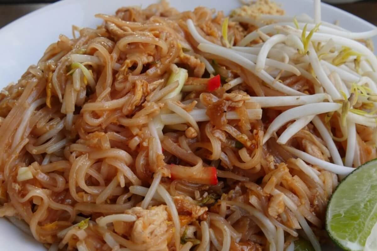A plate of Pad Thai with rice noodles, bean sprouts, chicken pieces, and red pepper slices, garnished with a lime wedge on the side. The noodles are lightly coated in a brown sauce, and the bean sprouts are placed on top for a fresh crunch—enjoyed at one of the best Thai restaurants in Metro Manila.