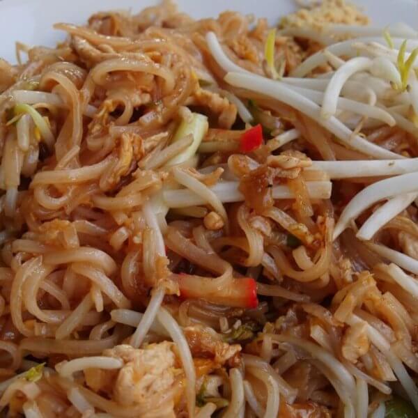 A plate of Pad Thai with rice noodles, bean sprouts, chicken pieces, and red pepper slices, garnished with a lime wedge on the side. The noodles are lightly coated in a brown sauce, and the bean sprouts are placed on top for a fresh crunch—enjoyed at one of the best Thai restaurants in Metro Manila.
