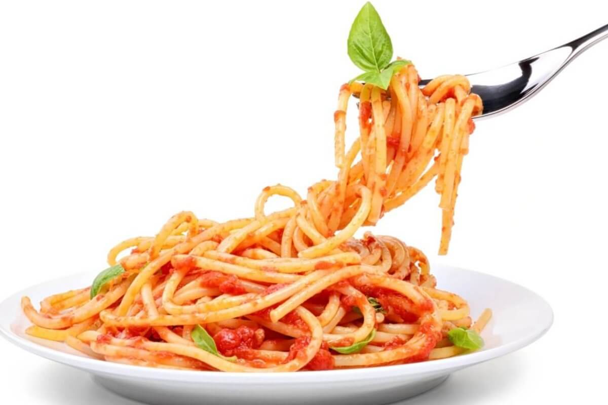 A fork twirls spaghetti topped with tomato sauce, garnished with a fresh basil leaf, lifted above a white plate filled with more spaghetti. The background is plain white, emphasizing the colorful dish—just like you'd experience at the best restaurants in One Ayala dining.