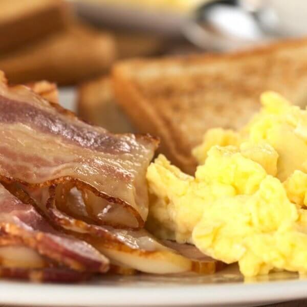 A breakfast plate from one of Marikina's top breakfast restaurants features fluffy scrambled eggs, several strips of crispy bacon with visible fatty edges, and golden brown toast with grill marks.