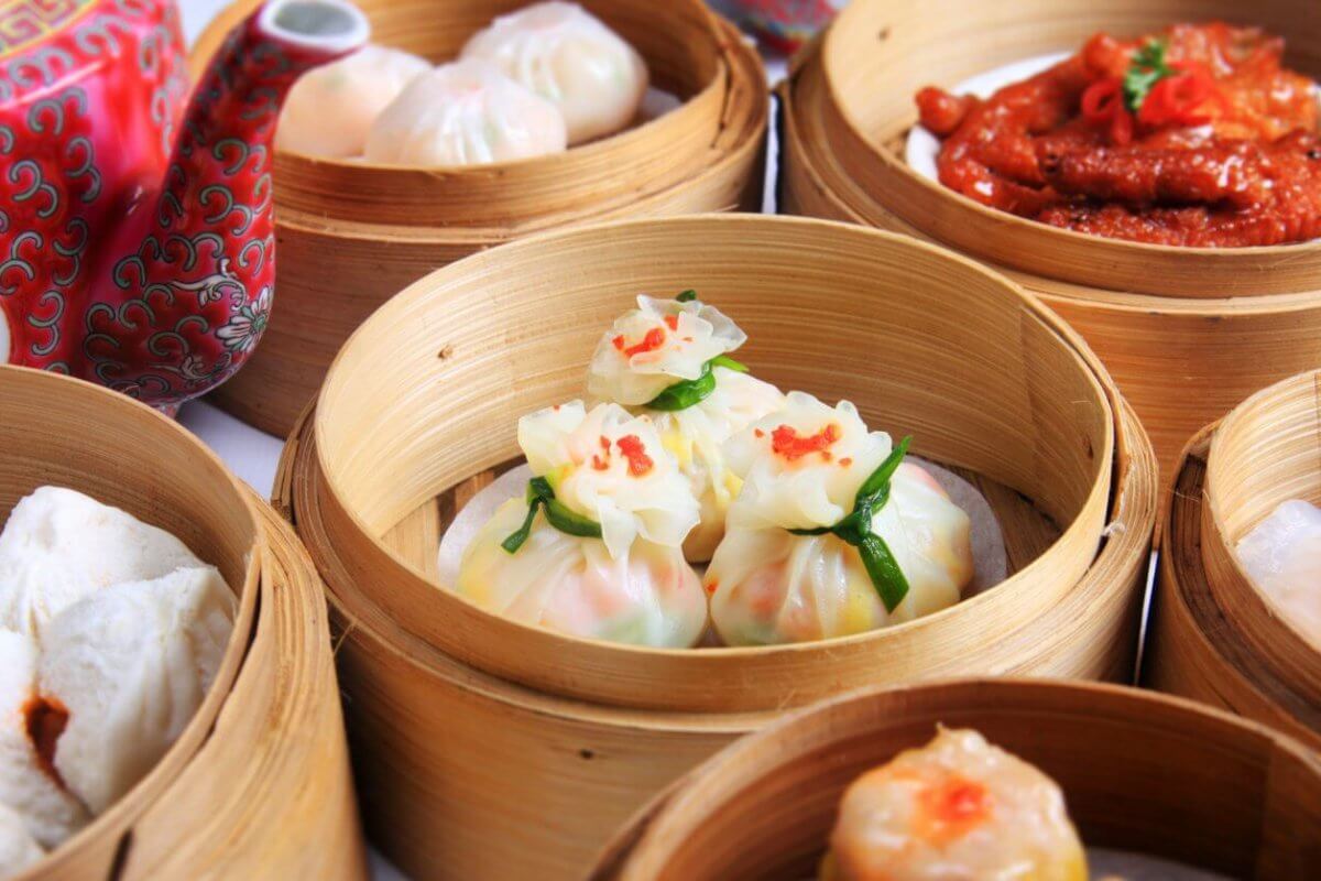 A variety of dimsum dishes are served in bamboo steamers. The dishes include dumplings, buns, and chicken feet. The dim sum items are intricately plated, with some garnished with a touch of red. A red, patterned teapot with Chinese characters is visible in the background—a typical scene in top 110 Chinese restaurants in Metro Manila.
