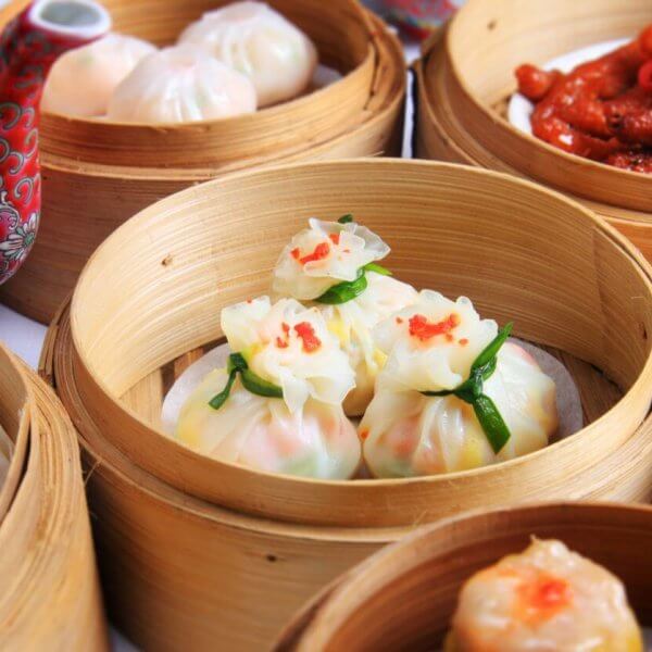 A variety of dimsum dishes are served in bamboo steamers. The dishes include dumplings, buns, and chicken feet. The dim sum items are intricately plated, with some garnished with a touch of red. A red, patterned teapot with Chinese characters is visible in the background—a typical scene in top 110 Chinese restaurants in Metro Manila.