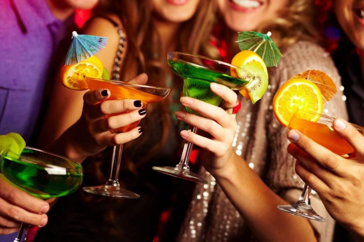A group of people holding colorful cocktails, each garnished with citrus slices and tiny umbrellas, toast together. The scene is lively, with the group smiling and dressed in festive attire, suggesting a celebratory occasion or party. Located in Poblacion, this hotspot ranks among 115 must-visit bars for every occasion.