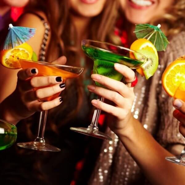 A group of people holding colorful cocktails, each garnished with citrus slices and tiny umbrellas, toast together. The scene is lively, with the group smiling and dressed in festive attire, suggesting a celebratory occasion or party. Located in Poblacion, this hotspot ranks among 115 must-visit bars for every occasion.