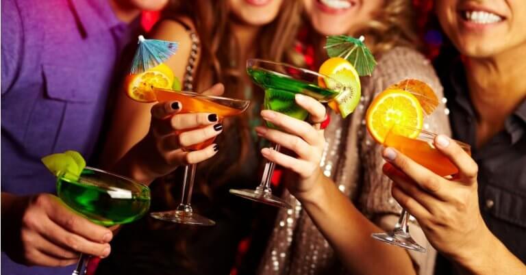 A group of people holding colorful cocktails, each garnished with citrus slices and tiny umbrellas, toast together. The scene is lively, with the group smiling and dressed in festive attire, suggesting a celebratory occasion or party. Located in Poblacion, this hotspot ranks among 115 must-visit bars for every occasion.